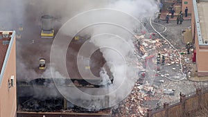 Aerial view of firefighters extinguishing fire in industrial or living area, near high office building after explosion