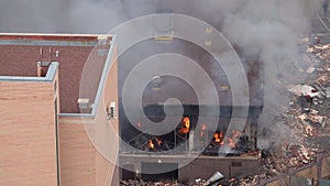 Aerial view of firefighters extinguishing fire in industrial or living area, near high office building after explosion