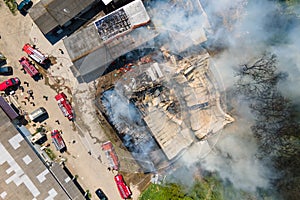 Aerial view of firefighters extinguishing ruined building on fire with collapsed roof and rising dark smoke