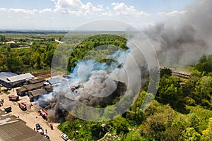 Aerial view of firefighters extinguishing ruined building on fire with collapsed roof and rising dark smoke