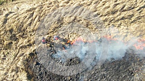 Aerial view of firemen extinguishing grassland field burning with red fire during dry season. Natural disaster and