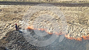 Aerial view of firemen extinguishing grassland field burning with red fire during dry season. Natural disaster and