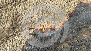 Aerial view of firemen extinguishing grassland field burning with red fire during dry season. Natural disaster and