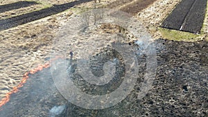 Aerial view of firemen extinguishing grassland field burning with red fire during dry season. Natural disaster and