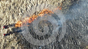 Aerial view of firemen extinguishing grassland field burning with red fire during dry season. Natural disaster and