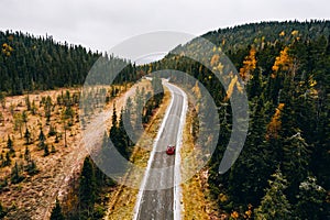 Aerial view of first snowy autumn color forest in the mountains and a road with car in Finland Lapland