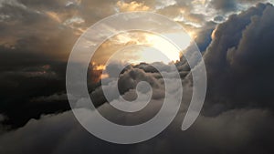 Aerial view flying through cumulus thunderclouds at sunset. Gold colored sunset cloudiness in high contrast. Real sky