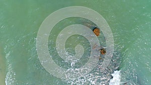 Aerial view flying over sea waves crashing rock at sea in summer