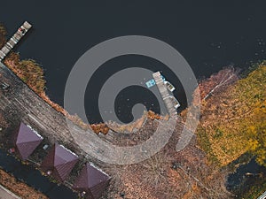 Aerial view of forest and blue lake. Sauna house by the lake shore. Wooden pier with fishing boats. St. Petersburg, Russia