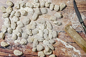Aerial view of fresh raw gnocchi on wooden background with a small knife and manual gnocchi maker