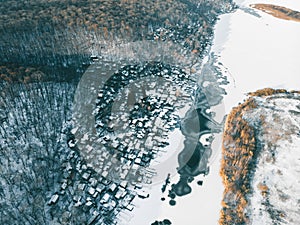 Aerial view of frozen river in snow and small village with houses and forest, view from drone as abstract winter background