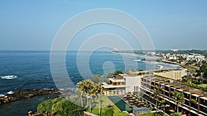 Aerial view of Galle Fort coastline. Lush greenery, historic architecture, Indian Ocean waves hit rocks. Clear sky