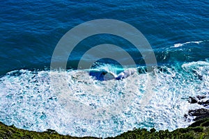 Aerial view of a giant ocean wave crushing onto the shore. Top down photo of turquoise sea water surface. White foam