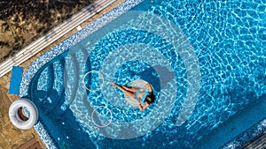 Aerial view of girl in swimming pool from above, kid swim on inflatable ring donut, fun in water on family vacation