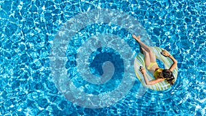 Aerial view of girl in swimming pool from above, kid swim on inflatable ring donut and has fun in water