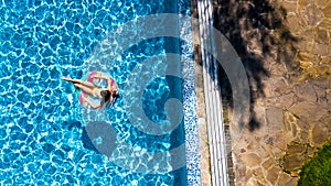 Aerial view of girl in swimming pool from above, kid swim on inflatable ring donut and has fun in water