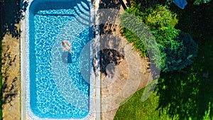 Aerial view of girl in swimming pool from above, kid swim on inflatable ring donut and has fun in water