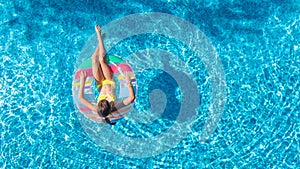 Aerial view of girl in swimming pool from above, kid swim on inflatable ring donut and has fun in water