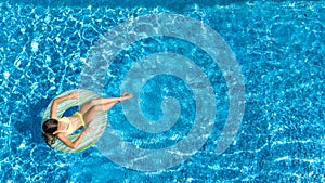 Aerial view of girl in swimming pool from above, kid swim on inflatable ring donut and has fun in water