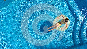 Aerial view of girl in swimming pool from above, kid swim on inflatable ring donut and has fun in water