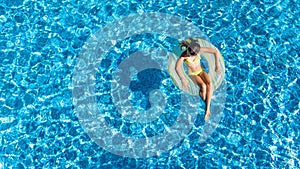 Aerial view of girl in swimming pool from above, kid swim on inflatable ring donut and has fun in water