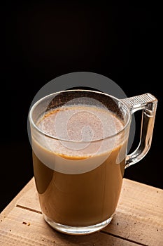 Aerial view of glass cup of coffee with milk, on wooden table, black background, vertical