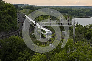 Aerial view of a GO train going through a forest area by a lake.