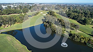 Aerial view of golf course dam with fountain surrounded by fairways, trees and bunkers