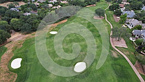 Aerial view of a golf course located in a city with lush trees surrounding the playing area