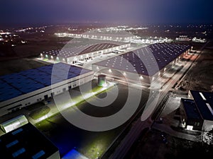 Aerial view of goods warehouse at Night. Logistics center in industrial city zone from above. Aerial view of trucks loading at