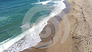 Aerial view of a gorgeous blonde woman walking on a beach. Sea waves washing sandy shoreline