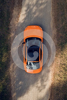 Aerial view of green forest and orange car on the road. Forest road going through forest with car adventure view from above