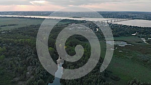 Aerial view of a green forest with a small river. Automobile bridge over the Dnieper river in the background