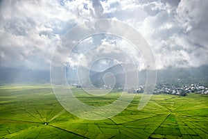 Aerial View of Green Lingko Spider Web Rice Fields with Sunlight Piercing Through Clouds to the Field with Raining. Flores, East N