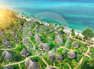 Aerial view of green palms, bungalows, grass, sandy beach, sea