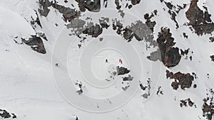 Aerial view. A group of skiers and snowboarders, high in the mountains, prepare for a steep descent along the snowy