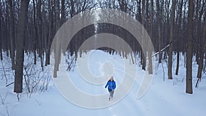 Aerial view on happy girl who runs around the snowdrifts in the forest. Scenic winter landscape