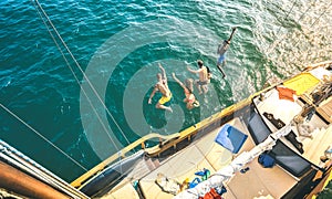 Aerial view of happy millenial friends jumping from sailboat on sea ocean trip - Rich guys and girls having fun together in