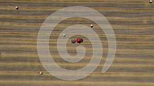 Aerial view of haymaking processed into round bales. Red tractor works in the field