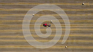 Aerial view of haymaking processed into round bales. Red tractor works in the field