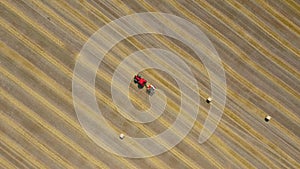 Aerial view of haymaking processed into round bales. Red tractor works in the field