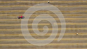 Aerial view of haymaking processed into round bales. Red tractor works in the field