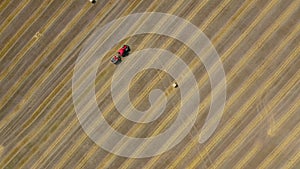 Aerial view of haymaking processed into round bales. Red tractor works in the field