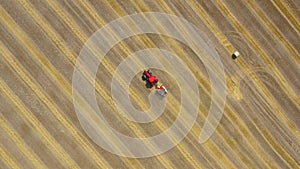 Aerial view of haymaking processed into round bales. Red tractor works in the field