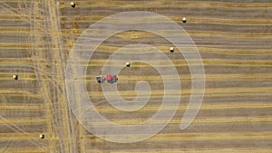 Aerial view of haymaking processed into round bales. Red tractor works in the field