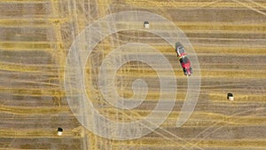Aerial view of haymaking processed into round bales. Red tractor works in the field