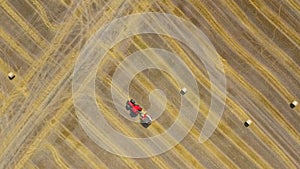 Aerial view of haymaking processed into round bales. Red tractor works in the field