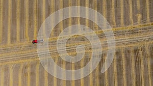 Aerial view of haymaking processed into round bales. Red tractor works in the field