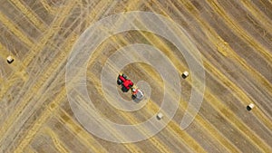 Aerial view of haymaking processed into round bales. Red tractor works in the field