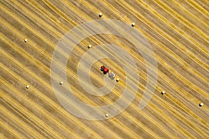 Aerial view of haymaking processed into round bales. Red tractor works in the field